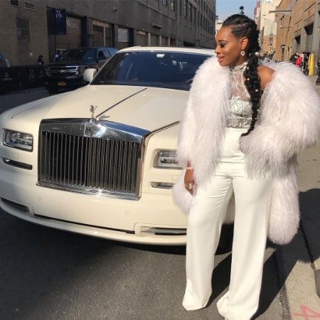 Yandy Smith wearing a white furry cloth in front of her white Rolls Royce 